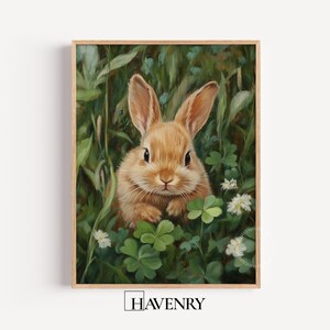 May include: A framed print featuring a brown rabbit amongst green foliage, clover, and small white flowers. The rabbit has long ears and a fluffy coat. The artwork has a natural, pastoral theme.