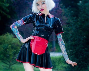 May include: A woman wearing a black latex dress with a red apron and black boots. She has white hair and tattoos on her arms.