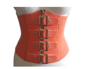 May include: Orange corset with a zipper closure and four buckle straps. The corset is made of a smooth material and is designed to cinch the waist. The metal hardware adds a touch of detail to the garment.