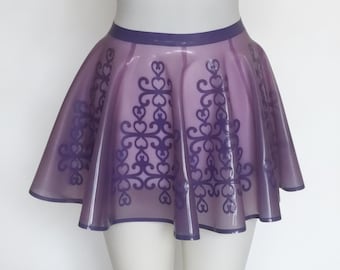 May include: A translucent light purple latex skater skirt featuring a dark purple filigree pattern with heart motifs. The skirt has a solid dark purple waistband and hemline, with a flared silhouette that falls above the knee on a mannequin.
