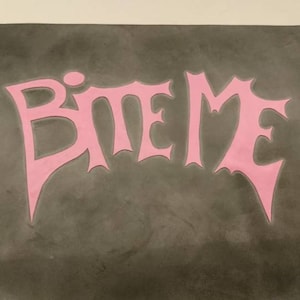 A black rubber mat with the words 'BITE ME' in pink lettering.