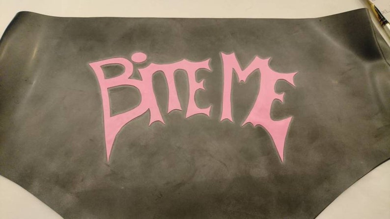 A black rubber mat with the words 'BITE ME' in pink lettering.
