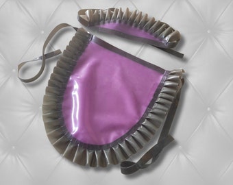 May include: A purple apron and matching headpiece set made of smooth, glossy material. The apron features a large, rounded central panel with wide, pleated dark gray ruffles along the edges and thin ties for securing the garment around the waist.