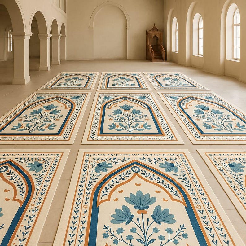 May include: An array of prayer rugs with a cream-colored background and a floral design in shades of blue and orange. The rugs are arranged in a large, open space with arched doorways and windows.