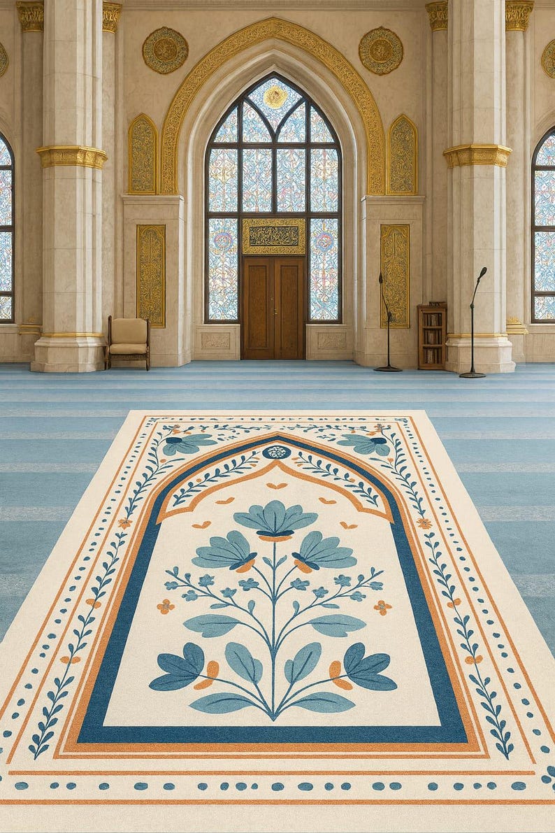 May include: An interior shot of a mosque featuring a prayer rug with a floral design in blue and orange. The rug is centered on a light blue carpet, with a large arched doorway and stained-glass windows in the background.