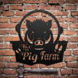 May include: Black metal sign with a circular frame featuring a wild boar design and the words "The Pig Farm". The sign is mounted on a red brick wall. A hammer rests below the sign.