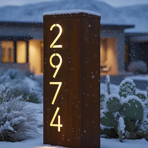 Peut inclure: Un panneau d'adresse rectangulaire en métal vieilli avec le numéro 2974 illuminé d'une lumière dorée et chaude. Le panneau est situé dans un paysage enneigé avec une maison en arrière-plan. Le panneau mesure environ 122 cm de haut.