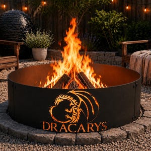 May include: A circular black metal fire pit ring featuring a laser-cut dragon silhouette and the text "DRACARYS" glowing from the flames within. The fire pit is constructed from multiple panels and sits on a bed of gravel in an outdoor space.
