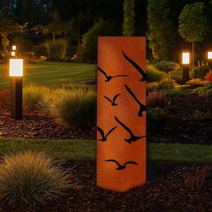 May include: A rectangular, weathered metal garden sculpture with a rusty orange finish. The sculpture features a series of black bird silhouettes cut out of the metal. The sculpture is placed in a garden setting with other decorative lights and landscaping.