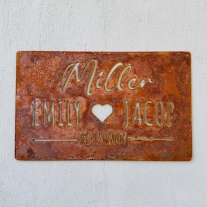May include: A rectangular, rusty metal sign with the names "Miller", "EMILY", and "JACOB" cut out. A heart shape is between the names. The date "08.15.2008" is also cut out.