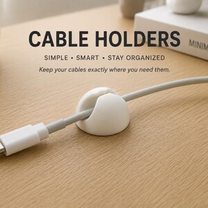 Op de afbeelding: Een witte, koepelvormige kabelhouder met een centrale gleuf, die een lichtgrijze USB-C-kabel vasthoudt. De tekst CABLE HOLDERS, SIMPLE • SMART • STAY ORGANIZED en Keep your cables exactly where you need them is zichtbaar boven de kabelhouder.
