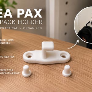 May include: A white plastic IKEA PAX backpack holder hook with two circular mounting holes and two separate white cylindrical caps. The text IKEA PAX BACKPACK HOLDER SIMPLE PRACTICAL ORGANIZED is visible along with icons indicating no drilling required.