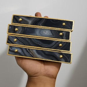 May include: Four rectangular cabinet pulls with a gold-colored frame and a black and gray agate stone center. Each pull has a single gold-colored stud. The pulls are stacked on top of each other.