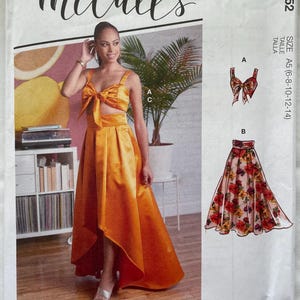 Puede incluir: Patrón de costura McCall's que muestra a una mujer con un vestido de satén naranja con top de lazo y falda asimétrica. El patrón incluye múltiples opciones de vista e instrucciones sencillas. El texto "McCall's" está en la parte superior y la talla es A5 (6-8-10-12-14).