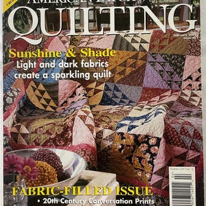 以下が含まれることがあります： 「American Patchwork & Quilting」誌の表紙には、幾何学模様のカラフルなキルトが掲載されています。雑誌のタイトルは大きな白い文字で、号のテーマである「Sunshine & Shade」と関連テキストが書かれています。表紙には号の発行日と価格も記載されています。