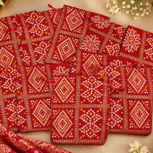 May include: A collection of rectangular red drawstring pouches featuring a repeating geometric pattern in white, orange, and yellow. Each pouch is accented with gold-toned embroidery along the grid lines and includes a red cord closure at the top.