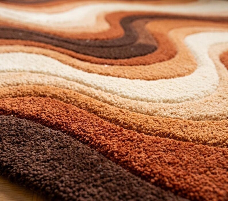 A close-up, angled view of the rug, showing the texture and wavy stripes in shades of brown, orange, and cream.