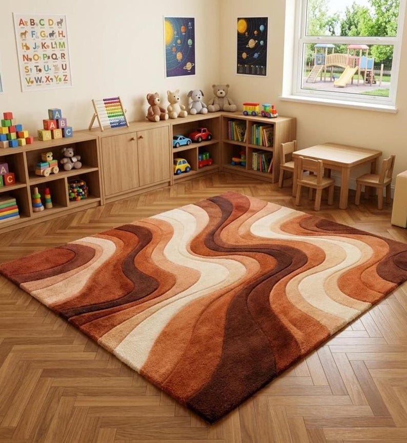 A rectangular rug with wavy stripes in shades of brown, orange, and cream on a light wood floor in a child's playroom with wooden furniture and toys.