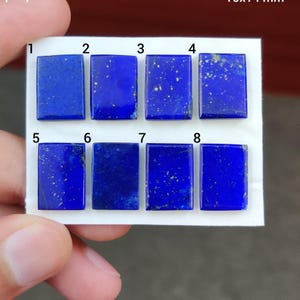 Peut inclure: Huit pierres précieuses rectangulaires en lapis-lazuli, chacune d'un bleu profond avec des éclats dorés. Les pierres sont disposées en deux rangées de quatre, présentées sur une surface blanche. Les pierres mesurent environ 10x14 mm.