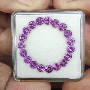 Könnte beinhalten: Eine Ansammlung runder, facettierter, violetter Edelsteine, die in einem Kreis in einem transparenten Kunststoffgehäuse angeordnet sind. Die Edelsteine haben einen leuchtenden Lilaton.
