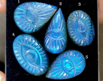 May include: Five carved blue labradorite gemstones, each with an eye design. The gemstones are in various shapes, including teardrop and oval. The carvings display detailed lines radiating from the eye, creating a unique aesthetic.