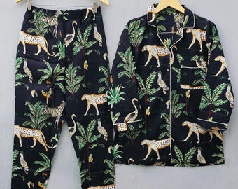 Könnte beinhalten: Schwarzes Pyjama-Set mit Dschungel-Print. Das Set besteht aus einem Hemd mit Knöpfen und einer Hose, beide mit einem Muster aus Leoparden, Vögeln und Palmen. Weiße Paspeln akzentuieren Kragen, Manschetten und Taschen des Hemdes. Auf Holzbügeln aufgehängt.