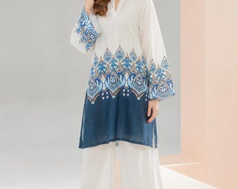 Könnte beinhalten: Eine weiße Tunika mit Stehkragen und langen Ärmeln, die ein blau-braunes dekoratives Muster im Mittelteil und an den Manschetten aufweist, kombiniert mit einer passenden weißen weiten Hose mit blau-braun gemustertem Saum.