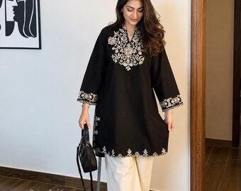 May include: A black long-sleeved tunic featuring intricate white embroidery around the neckline, cuffs, and hem, paired with wide-leg cream-colored trousers, brown strappy sandals, and a small black handbag. The text "style this kurta with me" is visible.