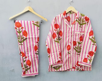 Könnte beinhalten: Ein zweiteiliges Pyjama-Set mit floralem Muster. Das Set besteht aus einem Hemd mit Knöpfen und einer Hose. Beide Teile haben einen rosa-weiß gestreiften Hintergrund mit roten Blumen und grünen Blättern.