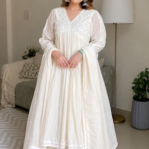 May include: An off-white long-sleeved dress featuring a V-neckline with intricate white floral embroidery on the bodice, a gathered waist, and a flowing skirt with a delicate lace trim along the hem, paired with a matching sheer dupatta scarf.