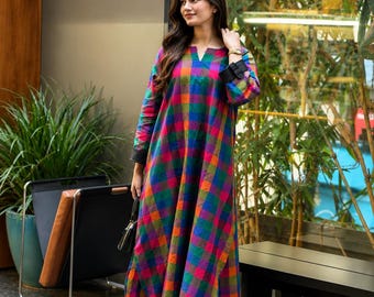 May include: A long-sleeved tunic featuring a vibrant multi-colored plaid pattern in shades of blue, green, orange, and magenta, with a notched neckline and solid black cuffs, paired with loose-fitting black trousers and brown open-toe sandals.