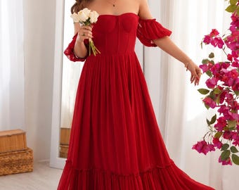 Könnte beinhalten: Ein bodenlanges rotes Kleid mit schulterfreiem Ausschnitt, kurzen Puffärmeln und einem strukturierten Oberteil im Korsett-Stil. Der Rock besteht aus fließendem, plissiertem Stoff mit einem gerüschten Saum, was eine volle und voluminöse Silhouette ergibt.