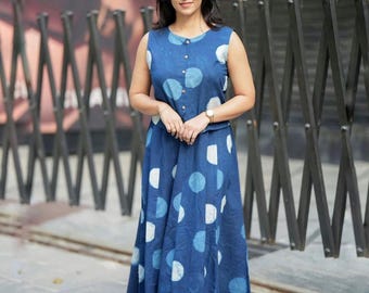 Könnte beinhalten: Ein ärmelloses, bodenlanges blaues Kleid mit einem weißen und hellblauen Polka-Dot-Muster. Das Kleid hat ein geknöpftes Oberteil und einen fließenden Rock. Die Frau trägt eine goldene Uhr und Sandalen.