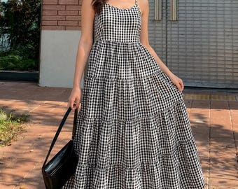 Könnte beinhalten: Ein bodenlanges, gestuftes Kleid mit schwarz-weißem Vichy-Karo-Muster, dünnen Spaghettiträgern und einem figurbetonten Oberteil. Das Kleid wird mit einer einfarbigen, schwarzen, rechteckigen Umhängetasche und einfachen schwarzen Riemchen-Flats kombiniert.