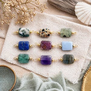 Peut inclure: Neuf connecteurs de pierres pr&eacute;cieuses de diff&eacute;rentes couleurs, dont le vert, le bleu, le violet et le marron mouchet&eacute;. Chaque pierre rectangulaire est reli&eacute;e par des boucles en m&eacute;tal dor&eacute;. Les pierres sont dispos&eacute;es sur un tissu de couleur neutre.