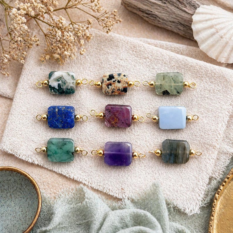 Peut inclure: Neuf connecteurs de pierres pr&eacute;cieuses de diff&eacute;rentes couleurs, dont le vert, le bleu, le violet et le marron mouchet&eacute;. Chaque pierre rectangulaire est reli&eacute;e par des boucles en m&eacute;tal dor&eacute;. Les pierres sont dispos&eacute;es sur un tissu de couleur neutre.