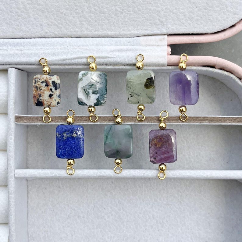 Peut inclure: Une collection de huit pendentifs en pierres pr&eacute;cieuses de diff&eacute;rentes couleurs et motifs. Chaque pierre rectangulaire est attach&eacute;e &agrave; une boucle en m&eacute;tal dor&eacute;. Les pierres pr&eacute;cieuses comprennent des vari&eacute;t&eacute;s marron mouchet&eacute;, blanc et vert, bleu et violet. Les pendentifs sont expos&eacute;s dans un &eacute;crin blanc.