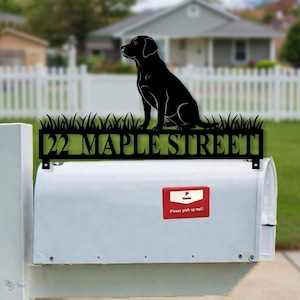 May include: Black metal mailbox topper featuring a silhouette of a Labrador dog sitting above a grassy design. The text "22 MAPLE STREET" is cut out below the dog. The mailbox is white with a red "Please pick up mail" sticker.