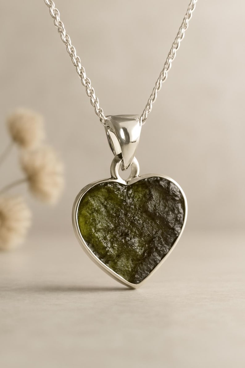 Peut inclure: Un collier pendentif en forme de c&oelig;ur avec une pierre vert olive textur&eacute;e sertie dans un cadre en m&eacute;tal argent&eacute;. Le pendentif est suspendu &agrave; une fine cha&icirc;ne argent&eacute;e, cr&eacute;ant un design simple mais &eacute;l&eacute;gant.