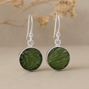 Peut inclure: Une paire de boucles d'oreilles en argent avec des pierres rondes, texturées, vert olive. Les boucles d'oreilles ont un design simple en forme de crochet et une finition polie, mettant en valeur la beauté naturelle des pierres précieuses.