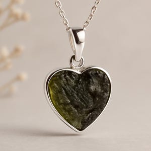 Peut inclure: Un collier en argent avec un pendentif en forme de c&oelig;ur. Le pendentif contient une pierre textur&eacute;e vert fonc&eacute;, encadr&eacute;e d'argent. La cha&icirc;ne est d&eacute;licate et argent&eacute;e, avec un fermoir simple.