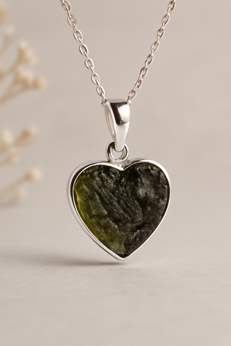 Peut inclure: Un collier en argent avec un pendentif en forme de c&oelig;ur. Le pendentif contient une pierre textur&eacute;e vert fonc&eacute;, encadr&eacute;e d'argent. La cha&icirc;ne est d&eacute;licate et argent&eacute;e, avec un fermoir simple.