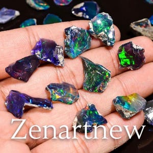 May include: A collection of raw opal gemstones in various shapes and sizes, displaying vibrant colors including blues, greens, and purples. The opals are held in a hand, with the text "Zenartnew" visible.