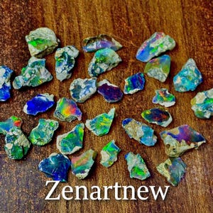 May include: A collection of raw opal gemstones with vibrant colors of blue, green, and purple. The rough stones are displayed on a wooden surface. The text "Zenartnew" is at the bottom of the image.
