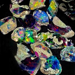 May include: A collection of iridescent opal gemstones in various shapes and sizes, displaying a spectrum of colors including blue, green, purple, and yellow. The opals are set against a black background, with the text "Zenartnew" at the bottom.
