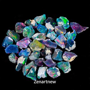 May include: A collection of raw opal gemstones with vibrant flashes of color, including blues, greens, and purples, against a black background. The opals are rough-cut, showcasing their natural textures and iridescence. The text "Zenartnew" is visible.