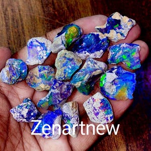May include: A collection of raw opals with vibrant blue, green, and purple iridescence. The rough stones have a natural, textured appearance, with a mix of colors and patterns. The text "Zenartnew" is visible at the bottom.