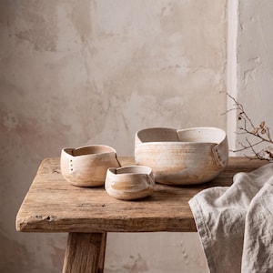 May include: Three ceramic bowls in varying sizes with a cream and tan marbled finish. Each bowl features a unique folded rim design with small punctured dot details along the edges, creating a cohesive set of handcrafted stoneware vessels.