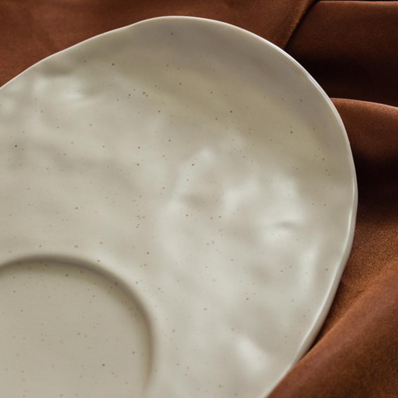 Close-up detail of speckled handmade ceramic saucer surface with soft organic texture