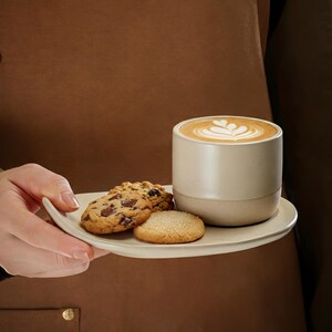 Close-up of ceramic coffee cup with latte art and cookies on a handcrafted stoneware plate